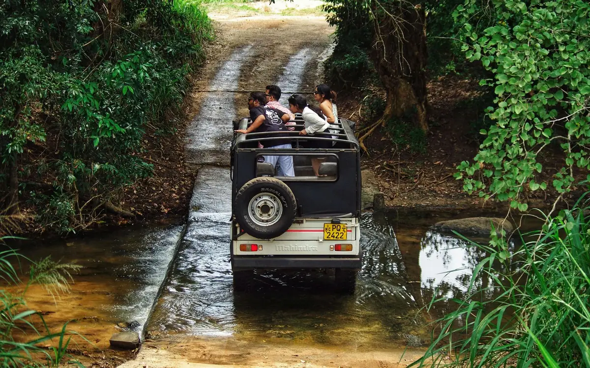 A safari jeep with travellers crossing a stream